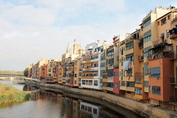 Fototapeta premium Colorful houses lining the Onyar River, Girona, Catalonia, Spain, a beautiful and historic European city with traditional architecture reflecting in the water under blue sky
