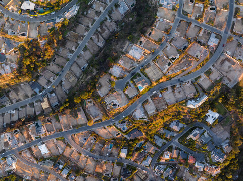 Aerial view of a suburban dreamscape where golden light bathes houses nestled along winding roads, casting deep shadows, Los Angeles, California, United States.