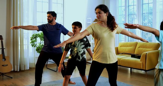 Indian family doing virabhadrasana yoga at home practicing warrior pose together indoors for healthy body and calm mind during morning routine inside a modern lavish living space