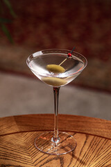 Clear martini style cocktail with olive served in stemmed glass on wooden table