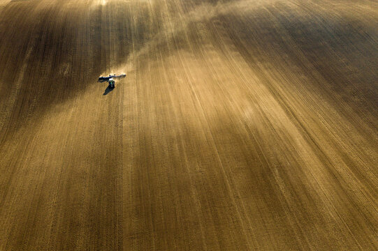 Aerial view of a lone tractor cutting through the field, its work leaving a trail of dust in the golden light, Svatoborice, Jihomoravsky kraj, Czechia.