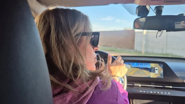 Woman driving screen displays parking assist features while maneuvering a modern car on a sunny day.