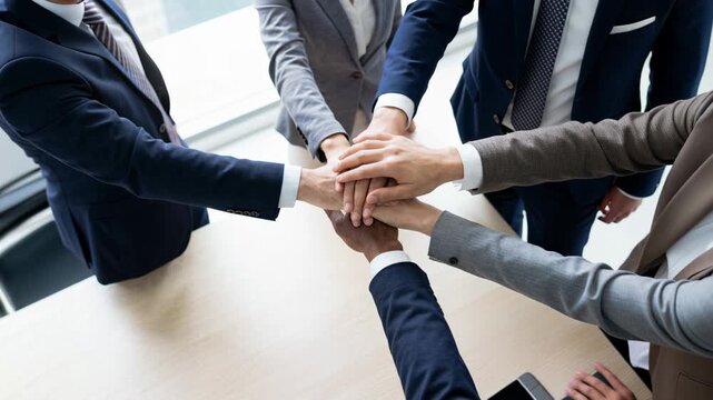 Business team stacking hands together symbolizing teamwork collaboration trust and corporate unity in boardroom with copy space.