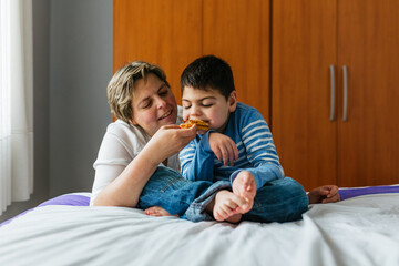Mother feeding son with microdeletion syndrome on bed