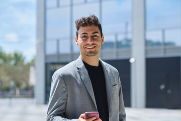 Young businessman smiling, holding phone in city lifestyle looking at camera confident © Cristina Garcia