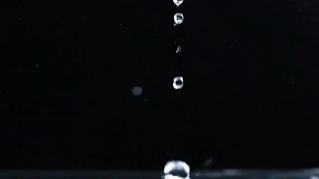 Occasional water droplets falling with faint trails on black minimalist cinematic background