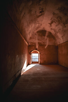 View of a dimly lit, stone chamber with a vaulted ceiling casting shadows, leading to a bright doorway framing the sea, Granada, Andalusia, Spain.