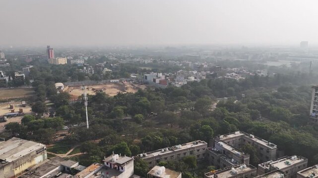 Aerial view of Greater Noida, showing low-rise residential clusters, green cover, and an active construction site under visible atmospheric haze typical of North Indian winters.