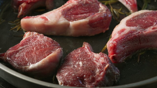 Raw lamb chops seasoned and arranged on pan with sprigs of rosemary before cooking, showing detailed texture and marbling of fresh uncooked meat