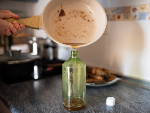Pouring used cooking oil from pan into green bottle for home recycling or environmental care campaign