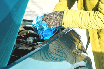 Pouring winter windshield washer fluid into car engine compartment