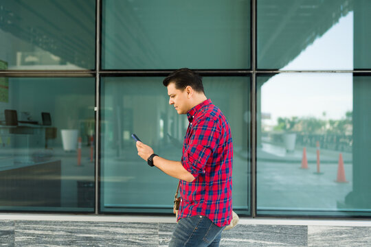 Profile view of a man walking, engrossed in mobile phone, ignoring surroundings in modern city environment