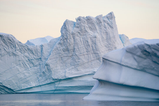 View of imposing icebergs, sculpted by time and the elements, float serenely in icy waters, a testament to nature's grandeur, Scoresby Sund, Greenland.