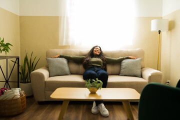 Obraz premium Young woman relaxing on comfortable sofa at home, feeling happy and peaceful, enjoying comfort in living room