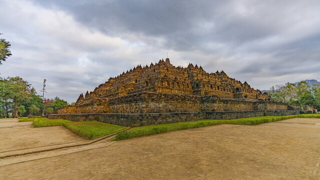 View of the majestic Borobudur temple stands in silent grandeur, its ancient stones whispering tales under a vast, cloud-strewn sky, Magelang, Central Java, Indonesia.