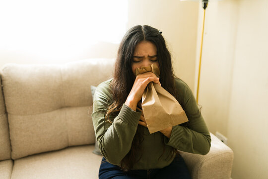 Adult woman having a panic attack, breathing into a paper bag to manage hyperventilation and anxiety