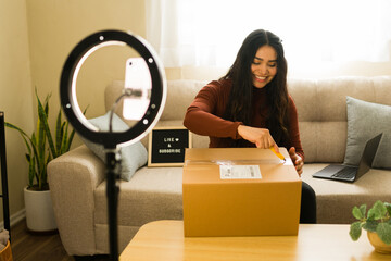 Woman creating unboxing video for social media channel, opening delivery package with ring light and smartphone
