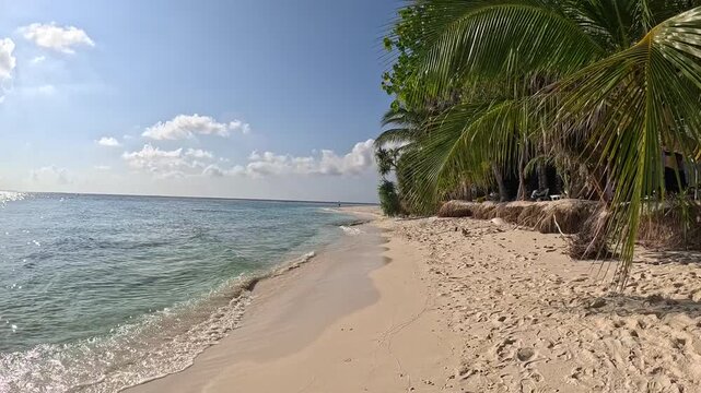 Person walking along white sand beach in Ukulhas Maldives with palm trees and turquoise water