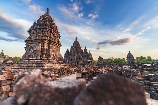 View of ancient stone temples rise majestically against a vibrant sky, casting shadows on the ruins in Prambanan, Daerah Istimewa Yogyakarta, Indonesia.