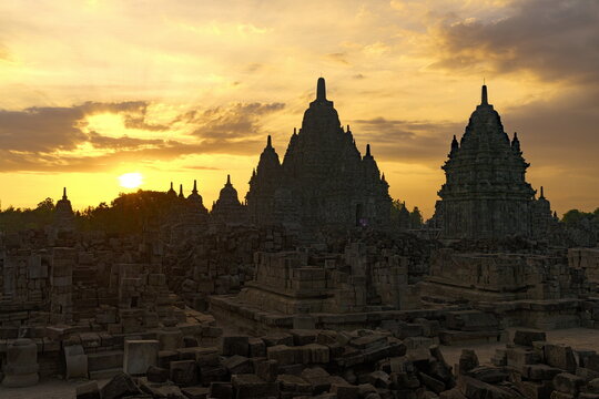 View of ancient temples rise silhouetted against a fiery sunset, casting long shadows across the weathered stones in Yogyakarta, Daerah Istimewa Yogyakarta, Indonesia.