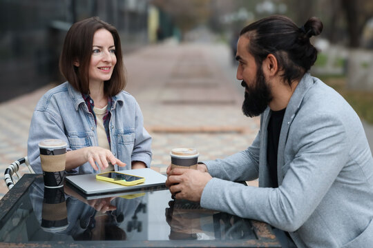Caucasian couple talking at outdoor cafe with coffee and laptop