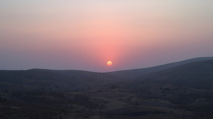 Obraz premium Crimson Horizon: A breathtaking vista unfolds as the sun dips below the horizon, painting the sky with a cascade of fiery hues and a tranquil desert scene.