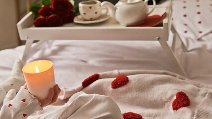 Romantic breakfast in bed with roses, tea, and a lit candle for Valentine's Day