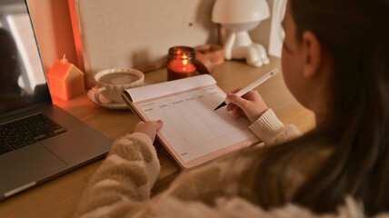 Young person writing in a weekly planner next to a laptop and coffee