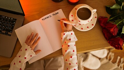 Overhead view of a person writing 'Today's Plan' in a notebook with a laptop and coffee