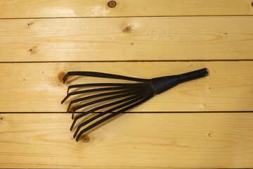 Metal rake head with multiple tines lies on wooden boards. Handle socket and bent tines visible in top view.