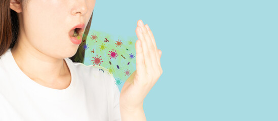Woman checking her oral with bad breath on blue background. Smelly mouth with bacteria and virus. Causes of halitosis include poor oral hygiene, foods and drinks, and health conditions. © Orawan