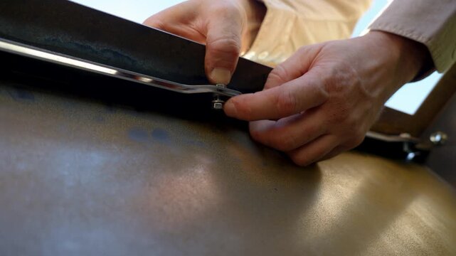 Close up of hands tightening a metal bolt, showing precision, craftsmanship, and work