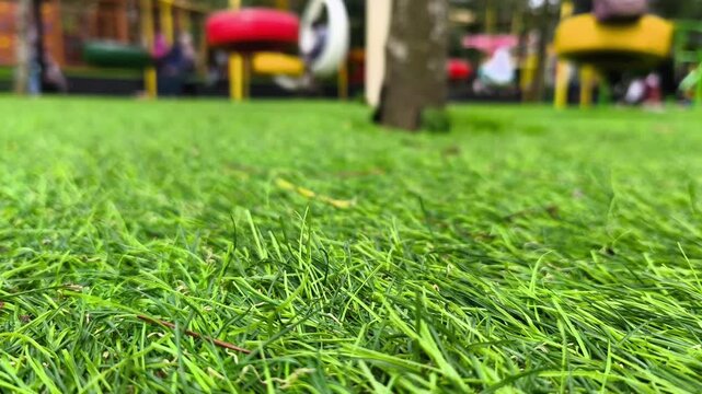 Green grass with blurred background of colorful swings in a playground that move slowly