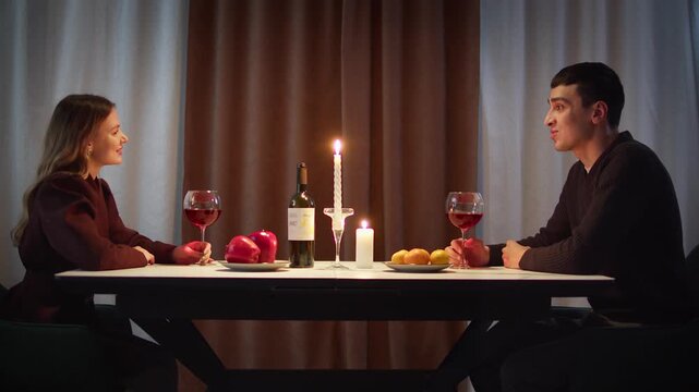 Couple have romantic candlelit dinner home, enjoying wine glasses and conversation. Date love night, anniversary celebration, casual evening gathering. Cozy candle light. Man and woman enjoy talking.