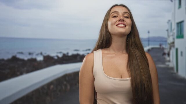 Woman smiling and showing cleavage with long hair on seaside street promenade, facing camera; vacation joy.