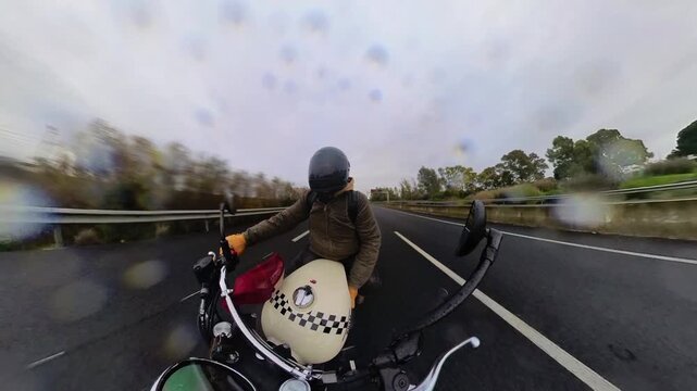 Toma en 4k de hombre conduciendo moto tipo scrambler mientras llueve por carretera