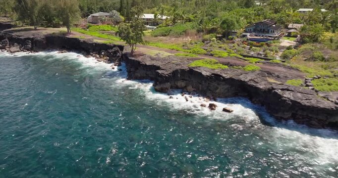 A strafing drone view of the popular Paradise Cliffs on the big island of Hawaii formed from ancient lava flows from the Kilauea volcano as waves crash on the dry magma with homes and vacation rentals