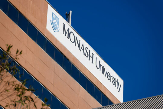 Large white Monash University sign, featuring black text and the institution's blue emblem, atop a building at the Caulfield campus, during the day
