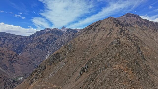 Drone slowly descends through Colca Canyon, focusing on towering mountains and dramatic geological formations rising from the canyon floor, showcasing raw power, scale, and ancient earth features.