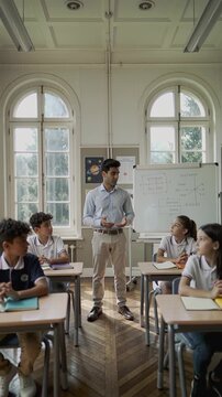 Male teacher explaining lesson to diverse school children in classroom. Education and learning during school day concept.
