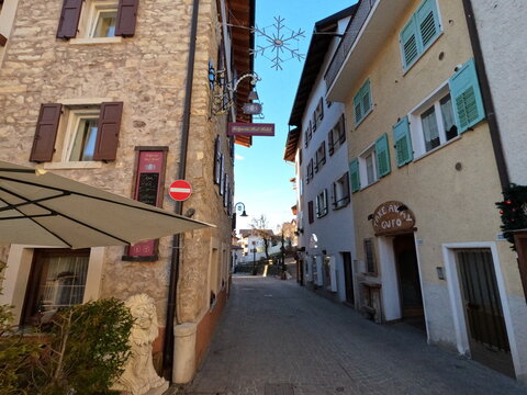  Stone Facade of Folgaria Post Hotel and Gufo Take Away Sign in Narrow Street with Christmas Decor Italy