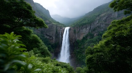 Fototapeta premium Majestic waterfall cascades powerfully down a steep green covered cliff face into a misty mountain valley