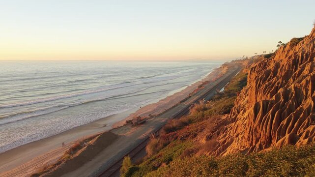Sunset illuminates the sandstone cliffs at Torrey Pines in Del Mar, California. People walk on the beach.