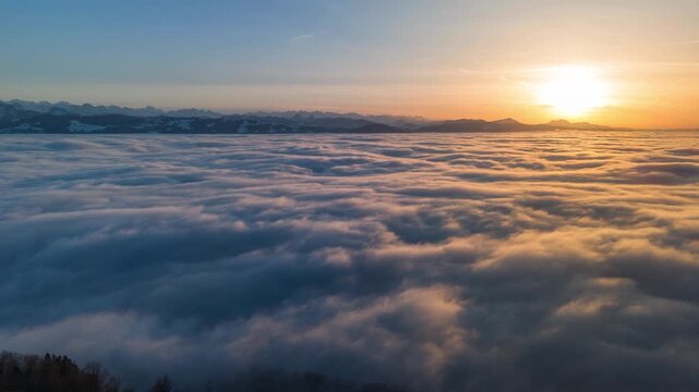 A time-lapse drone flight over the Swiss Alps with a sea of ​​fog below. Aerial view above the clouds. Sunset with a mountain backdrop. Beautiful natural landscape. Hyperlapse in winter.