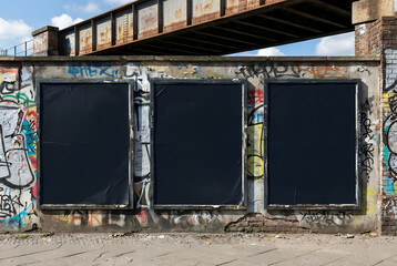 Three vertical blank black posters mockup on a colorful graffiti wall under an industrial bridge structure