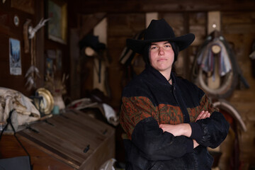 Obraz premium Cowgirl in a hat stands with arms crossed inside a rustic ranch workshop