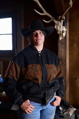 Cowgirl in a wide brimmed hat stands confidently in a rustic ranch interior