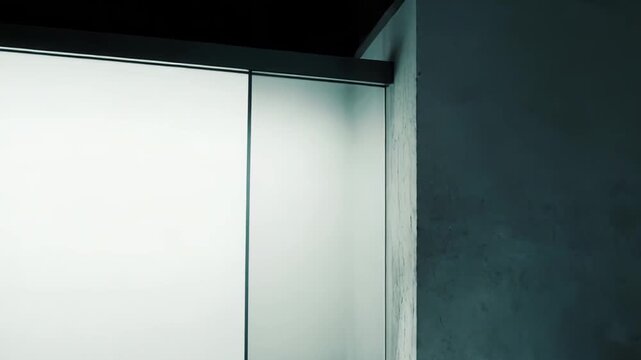 Frosted glass panel with diffused light effect forming a border next to a dark, textured concrete wall, creating an abstract background with contrast and gradient