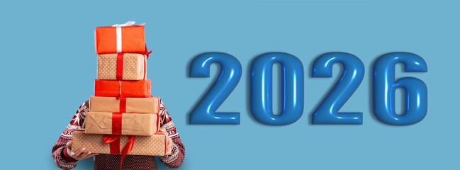 Obraz premium A person holds a stack of colorful gifts next to the large numbers representing the year 2026. This scene captures the spirit of celebration and togetherness.