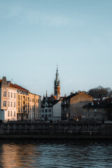 Fototapeta premium Historic city architecture along riverbank at sunset, urban landscape with old buildings and calm water reflection.